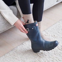 Person putting on a navy rain boot indoors
