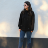 Woman wearing a black hoodie and blue jeans standing against a light-colored wall.