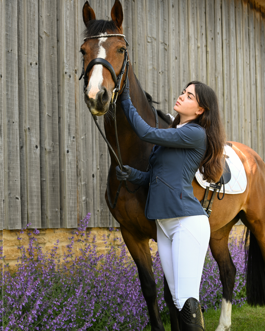 Woman petting a brown horse in front of a wooden fence with lavender flowers.