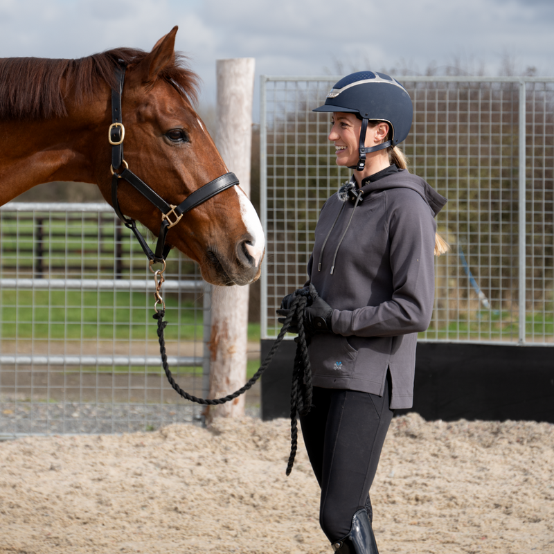 Woman in equestrian gear standing next to a horse in an outdoor setting