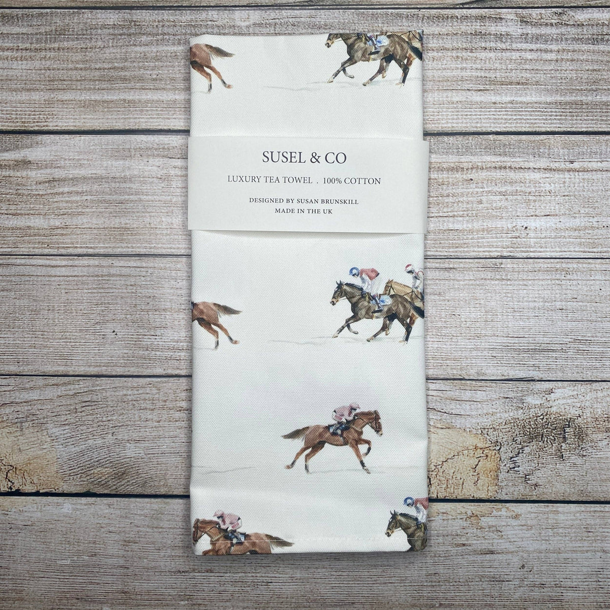 Tea towel with horse and jockey design on a wooden surface, featuring the brand 'SUSEL & CO'.