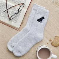 Gray socks with a black dog design on a wooden surface with a book, glasses, and mug.