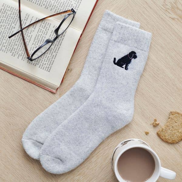 Gray socks with a black dog design on a wooden surface with a book, glasses, and mug.