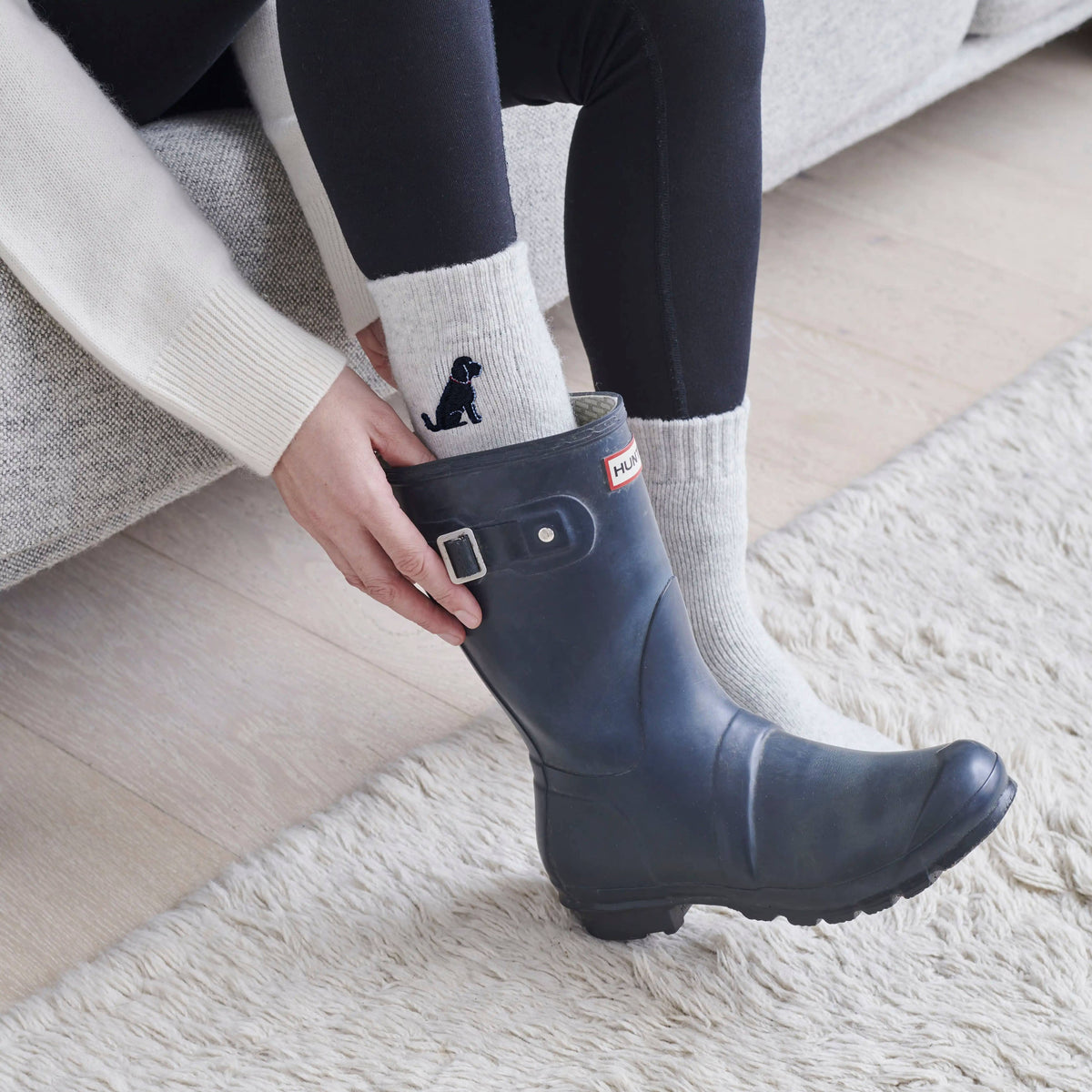 Person wearing navy rain boots with a white sock featuring a black silhouette, on a light wooden floor.