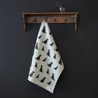 Tea towel with black dog pattern hanging on a wooden shelf against a dark wall.